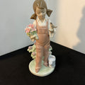 Porcelain figurine of a girl holding flowers and a bird on a black surface with a white background