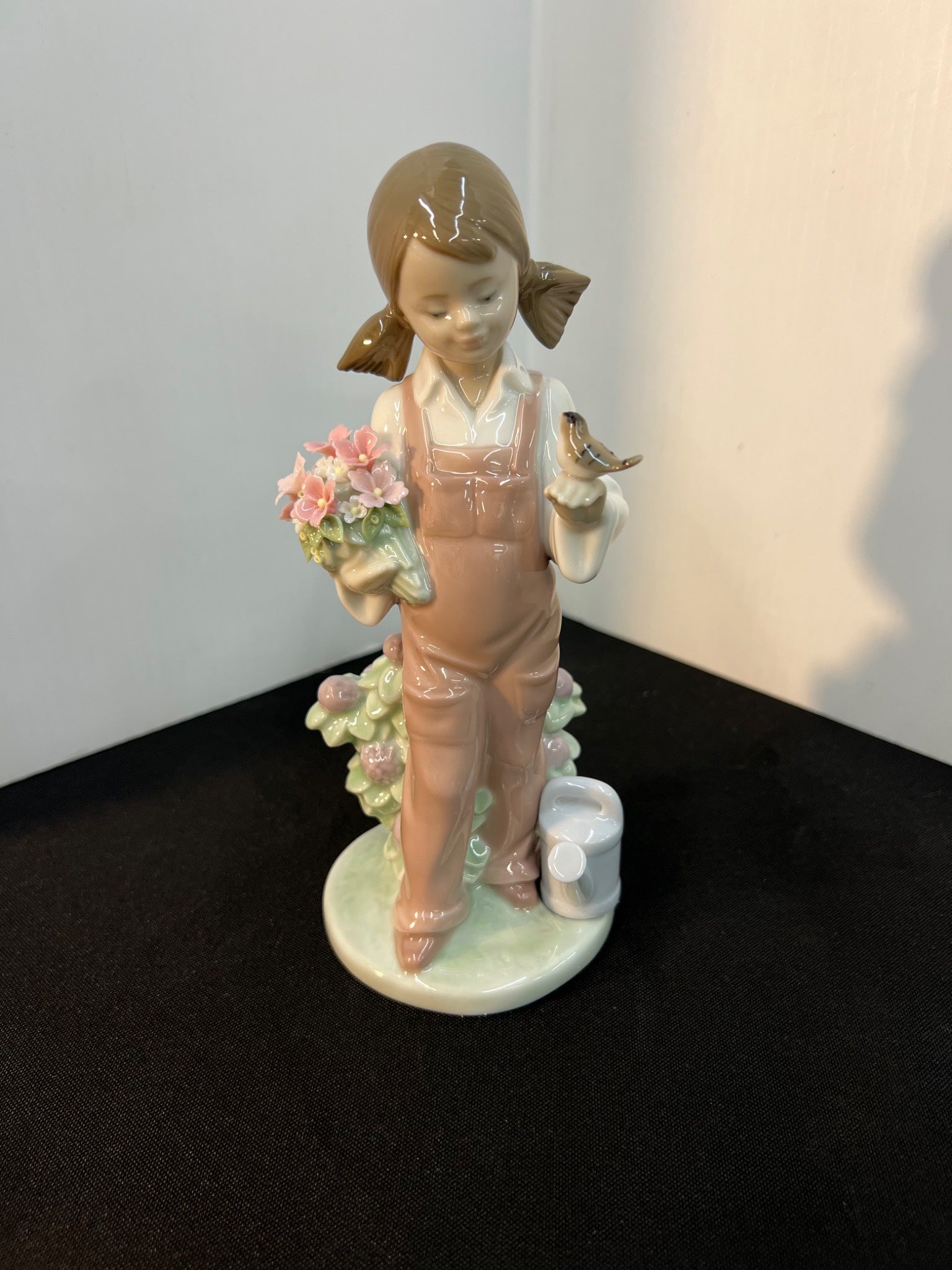 Porcelain figurine of a girl holding flowers and a bird on a black surface with a white background