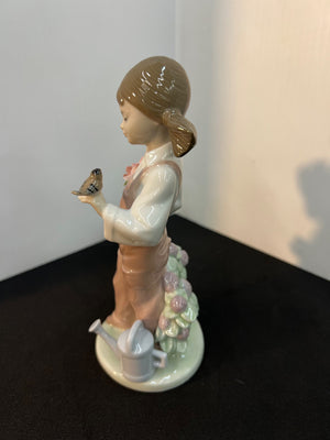 Porcelain figurine of a girl with a bird and flower arrangement on a dark surface.