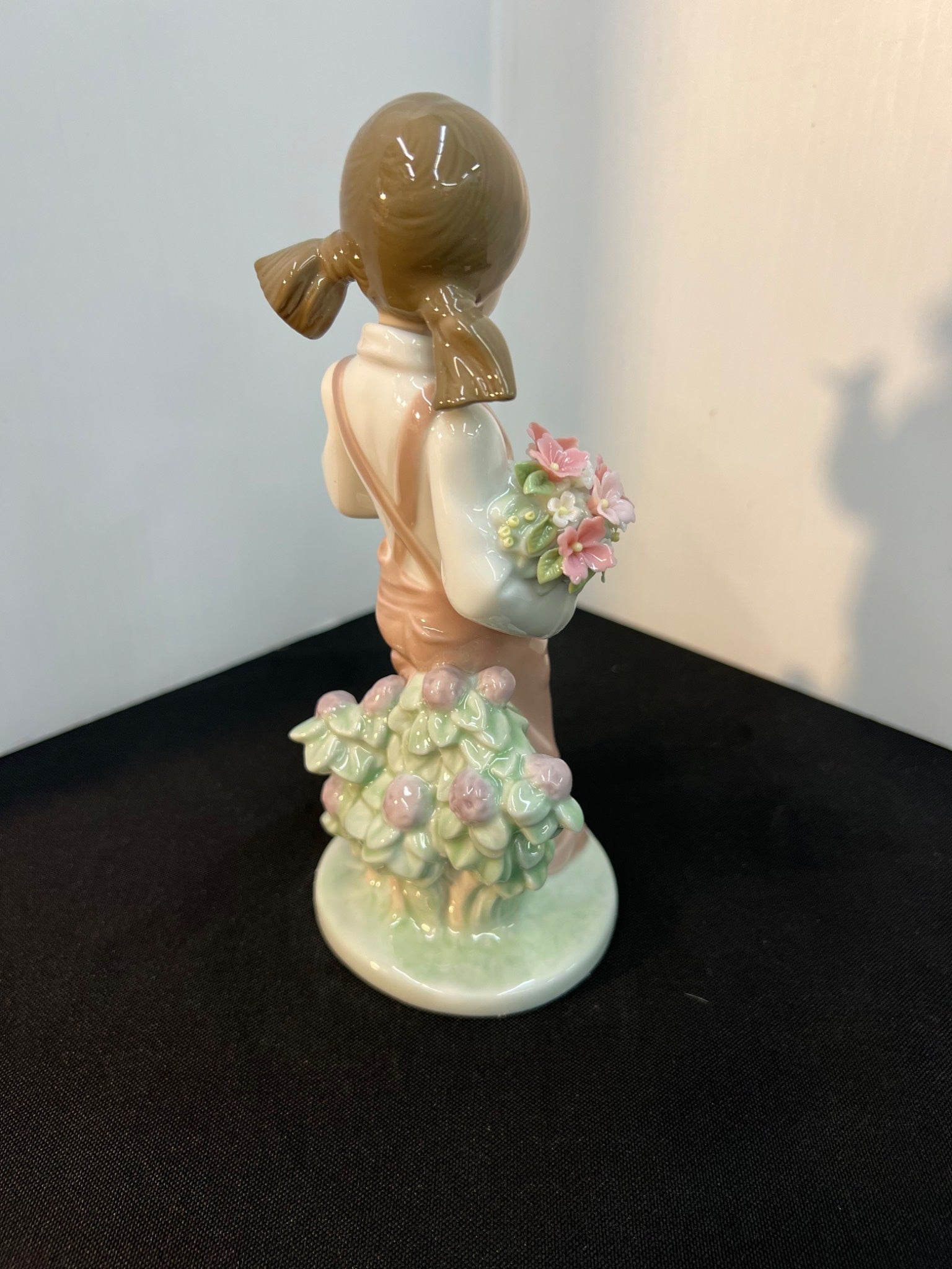 Porcelain figurine of a girl holding flowers on a black surface with a white wall background