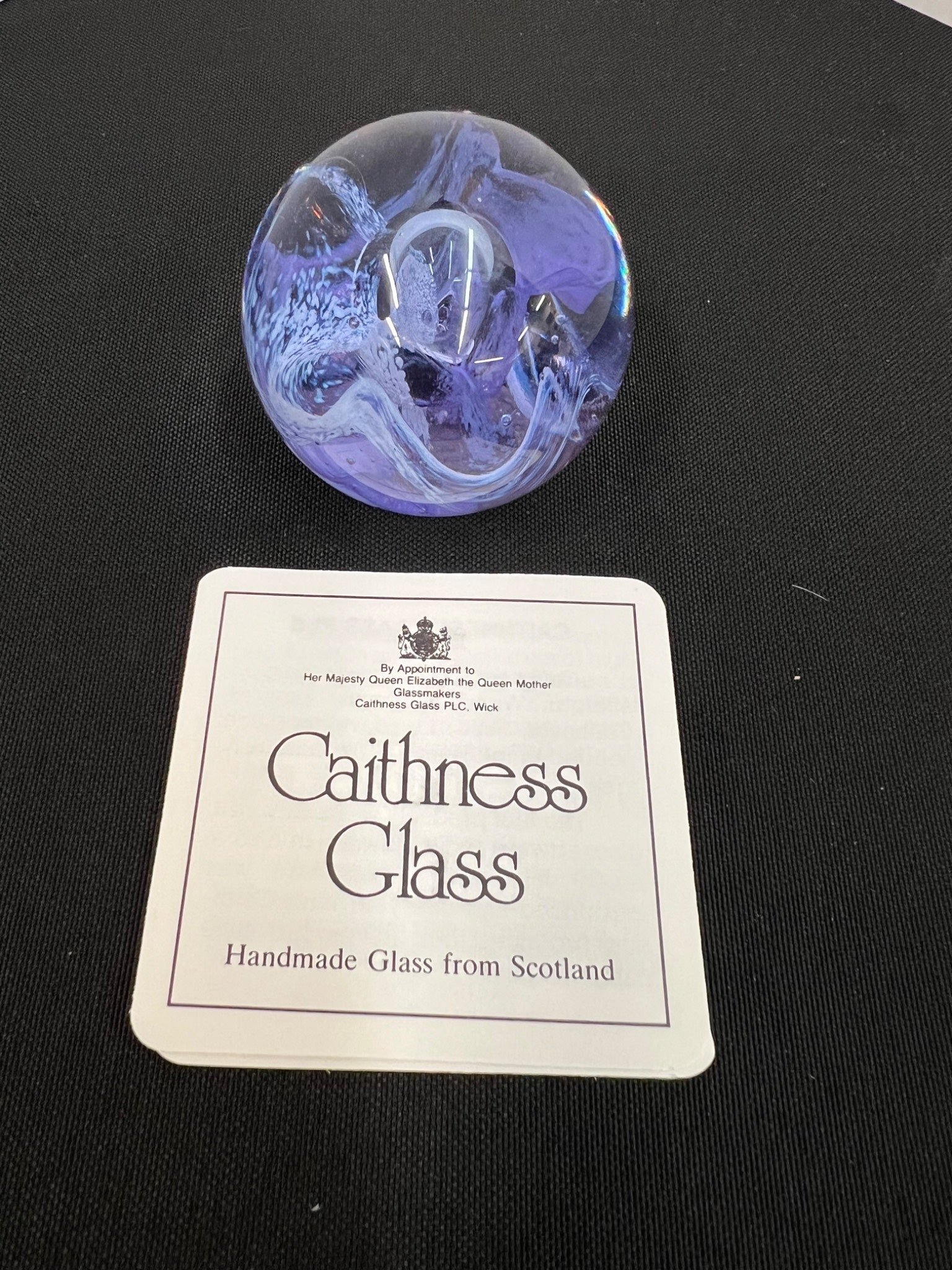 Purple glass paperweight with Caithness Glass label on a black background