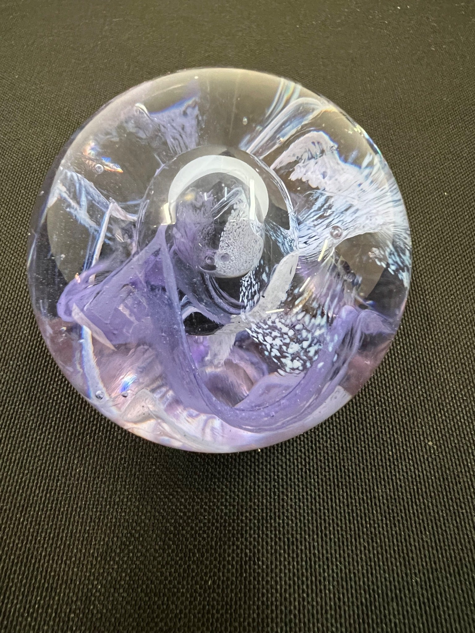Decorative glass paperweight with purple and white design on a dark surface