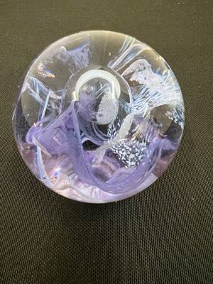 Decorative glass paperweight with purple and white design on a dark surface