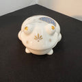 White ceramic frog-shaped container with decorative elements on a black surface.