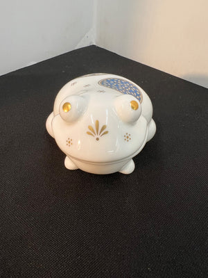 White ceramic frog-shaped container with decorative elements on a black surface.