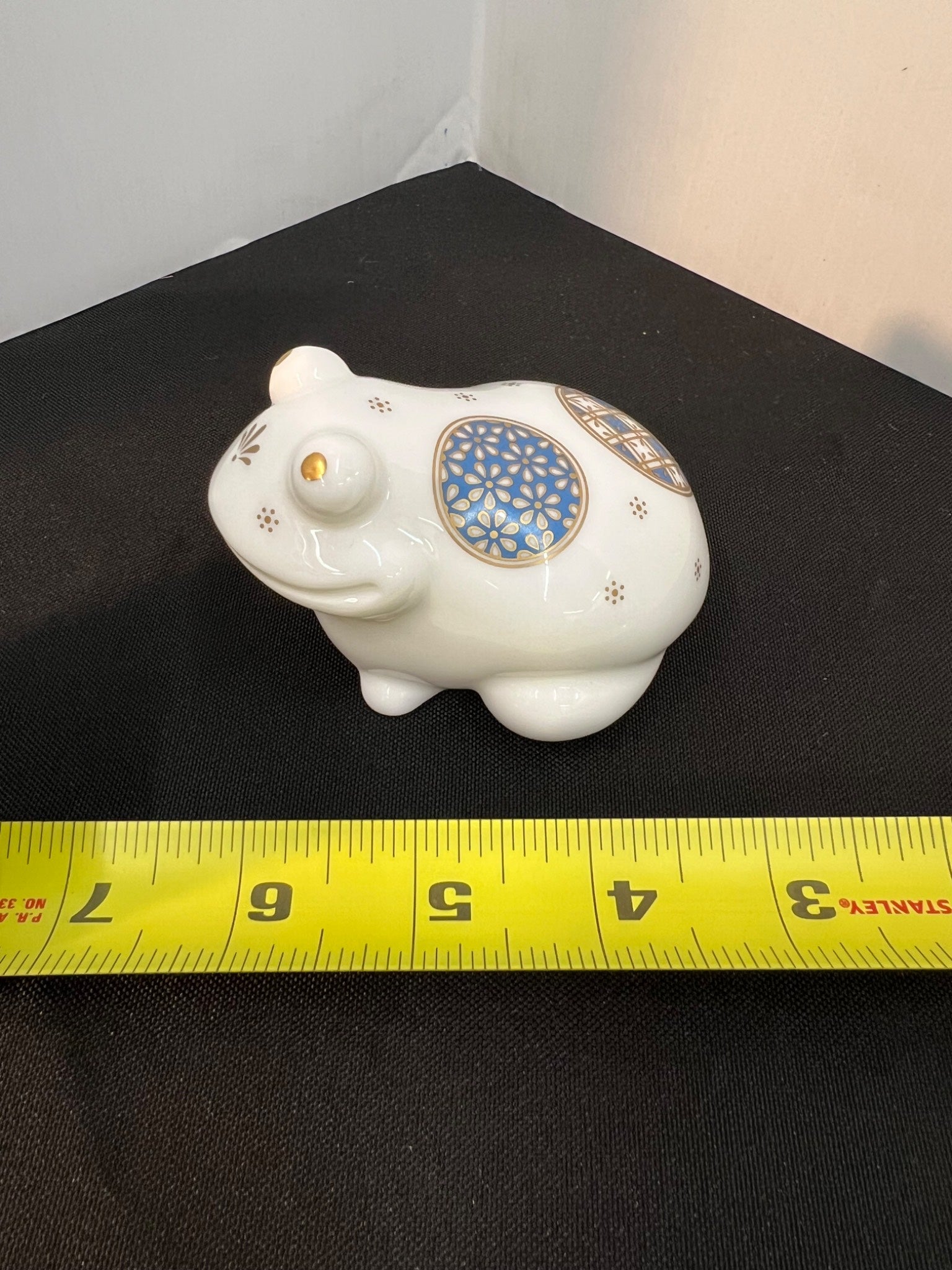 Decorative white piggy bank with blue circular design on a black surface, measured by a yellow tape measure.