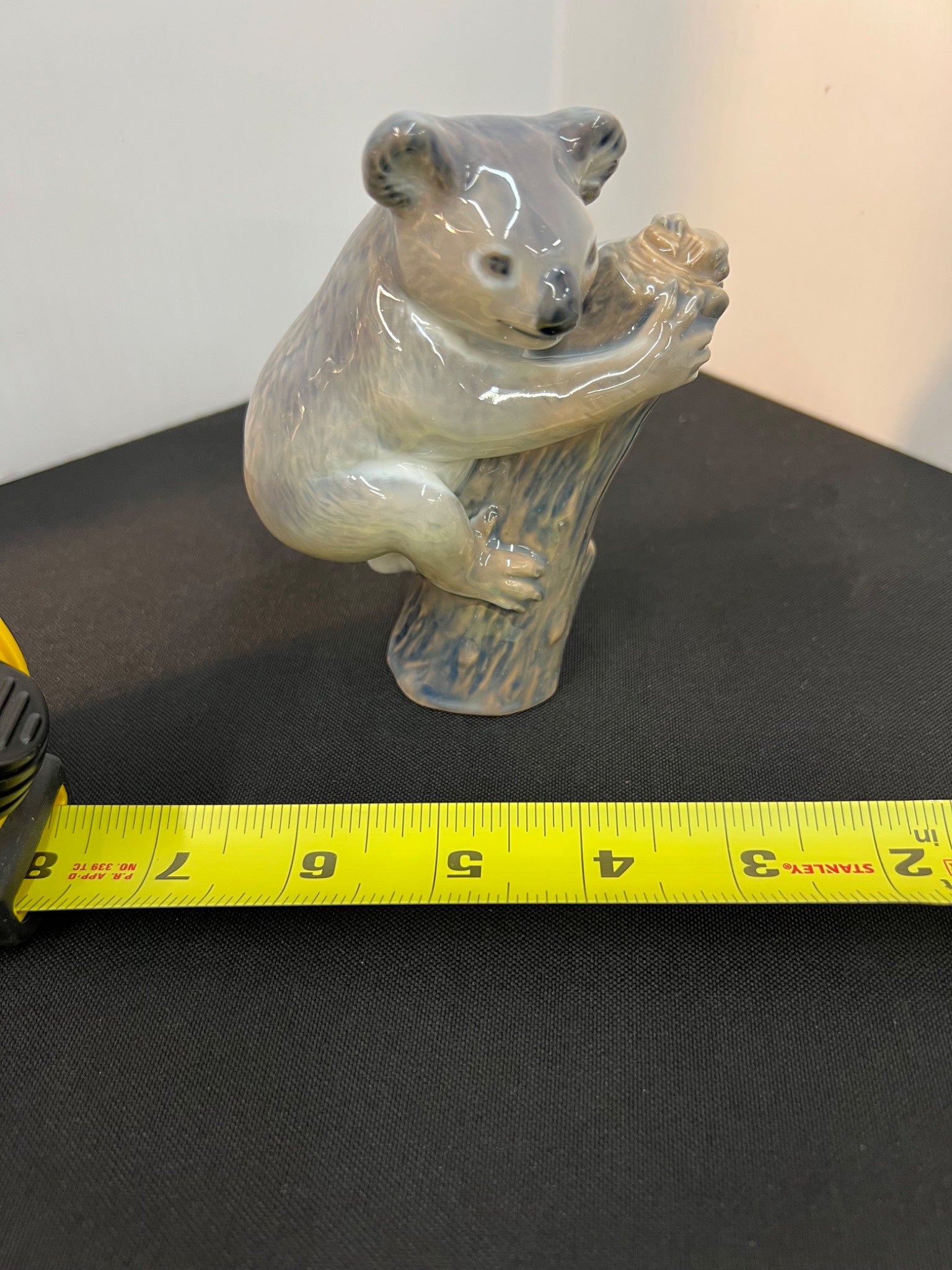 Bear figurine on a stand with a measuring tape for scale on a dark surface.