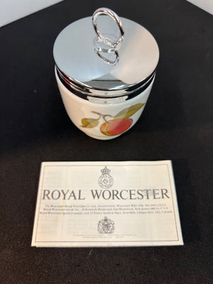 Decorative ceramic jar with silver lid on a black surface, accompanied by a Royal Worcester label.