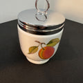 Small ceramic jar with a silver lid and fruit design on a black surface