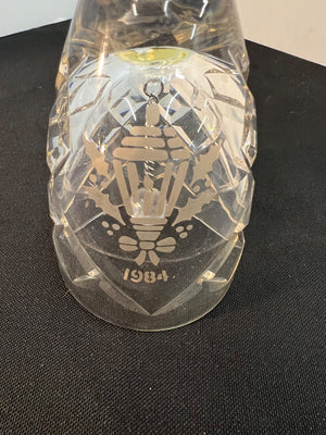 Clear glass ornament with intricate design and '1984' engraving on a black surface