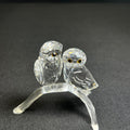 Glass sculpture of two owls on a branch against a dark background