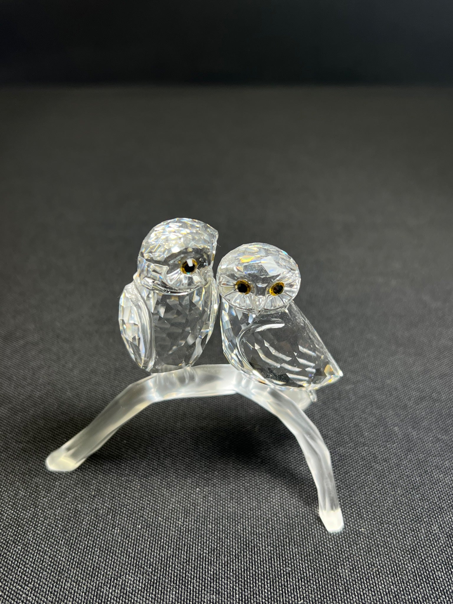 Glass sculpture of two owls on a branch against a dark background