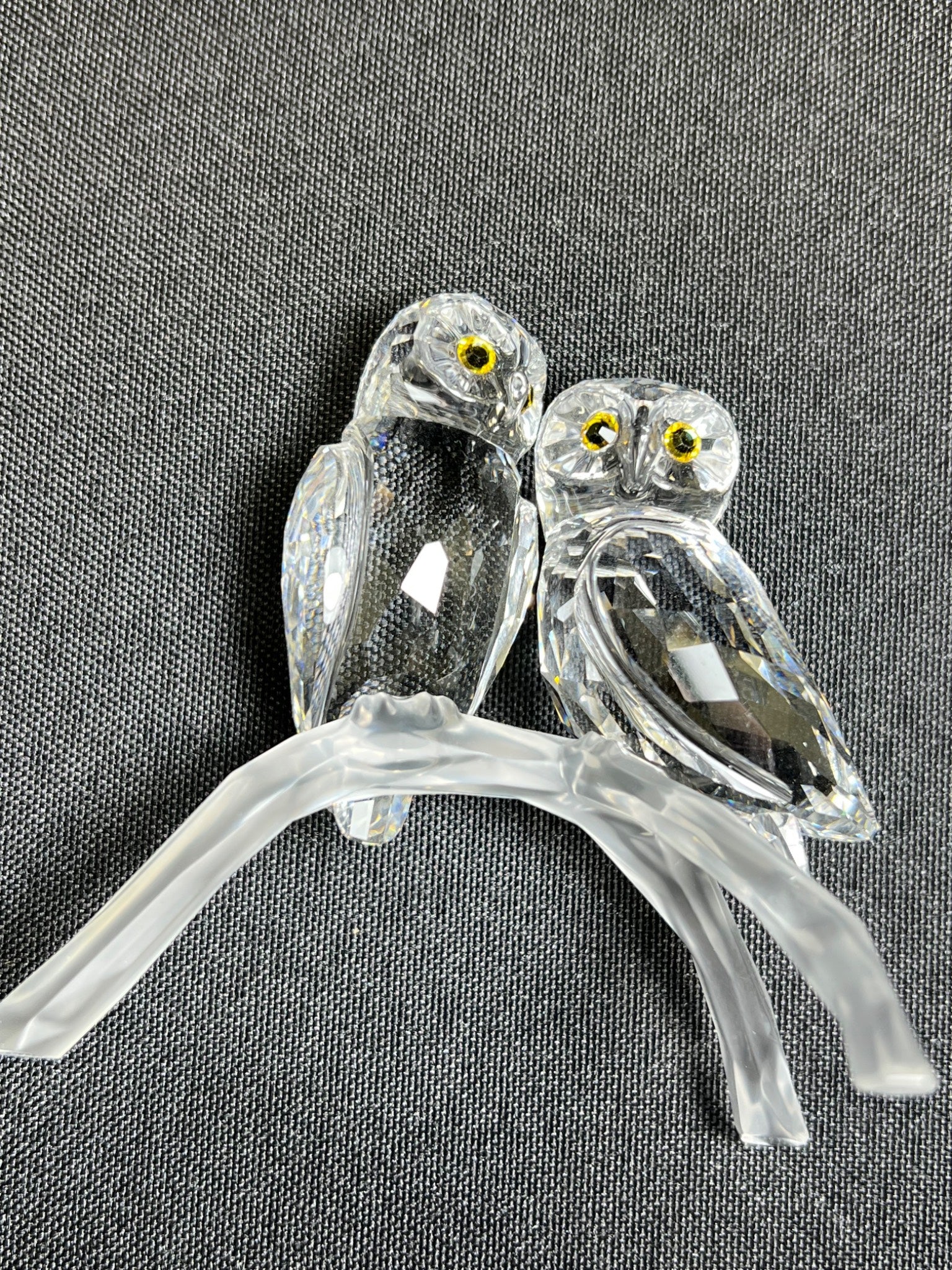 Two glass owls on a branch against a gray background