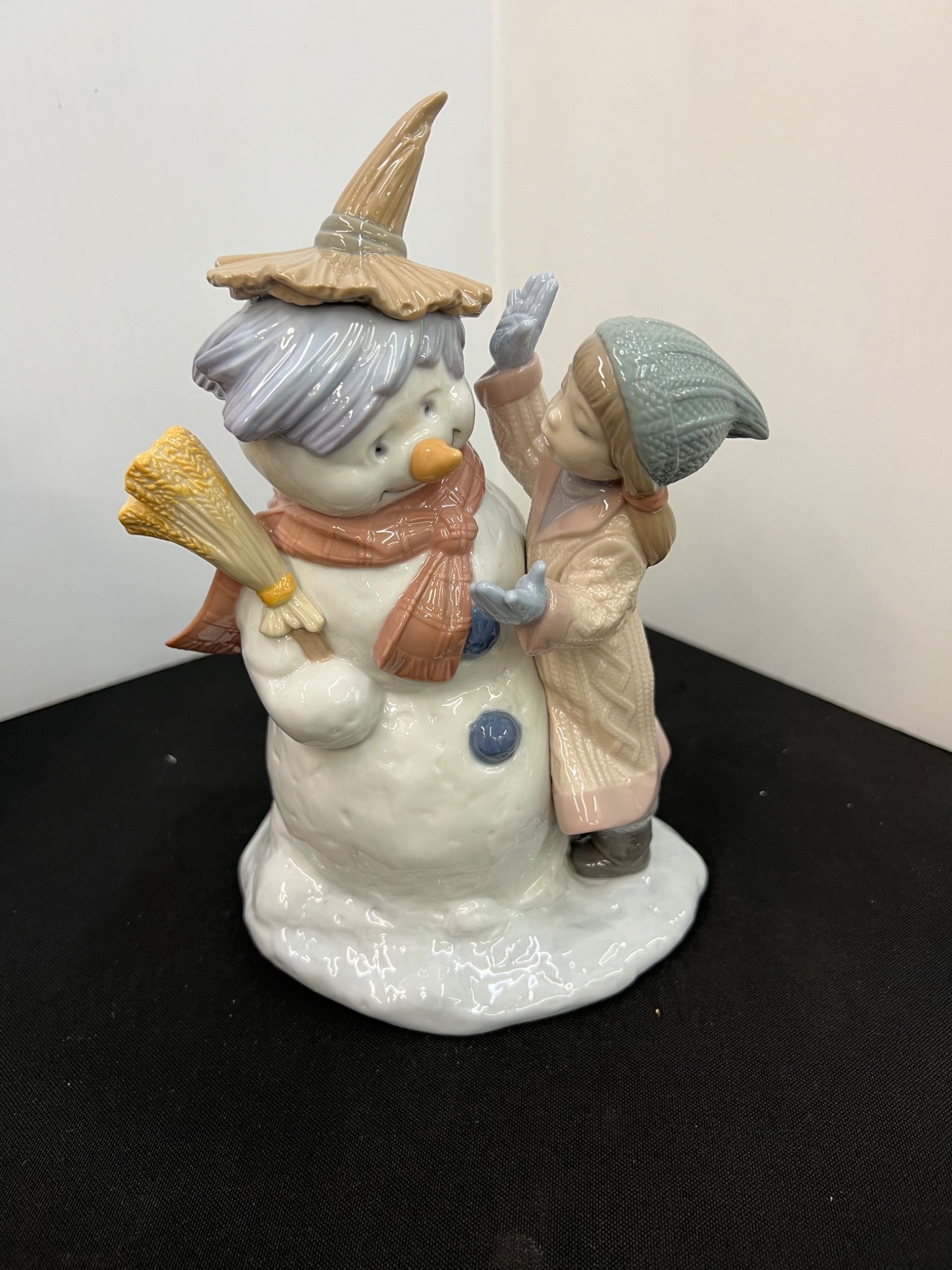 Snowman figurine with a child holding a blue bird on a black surface