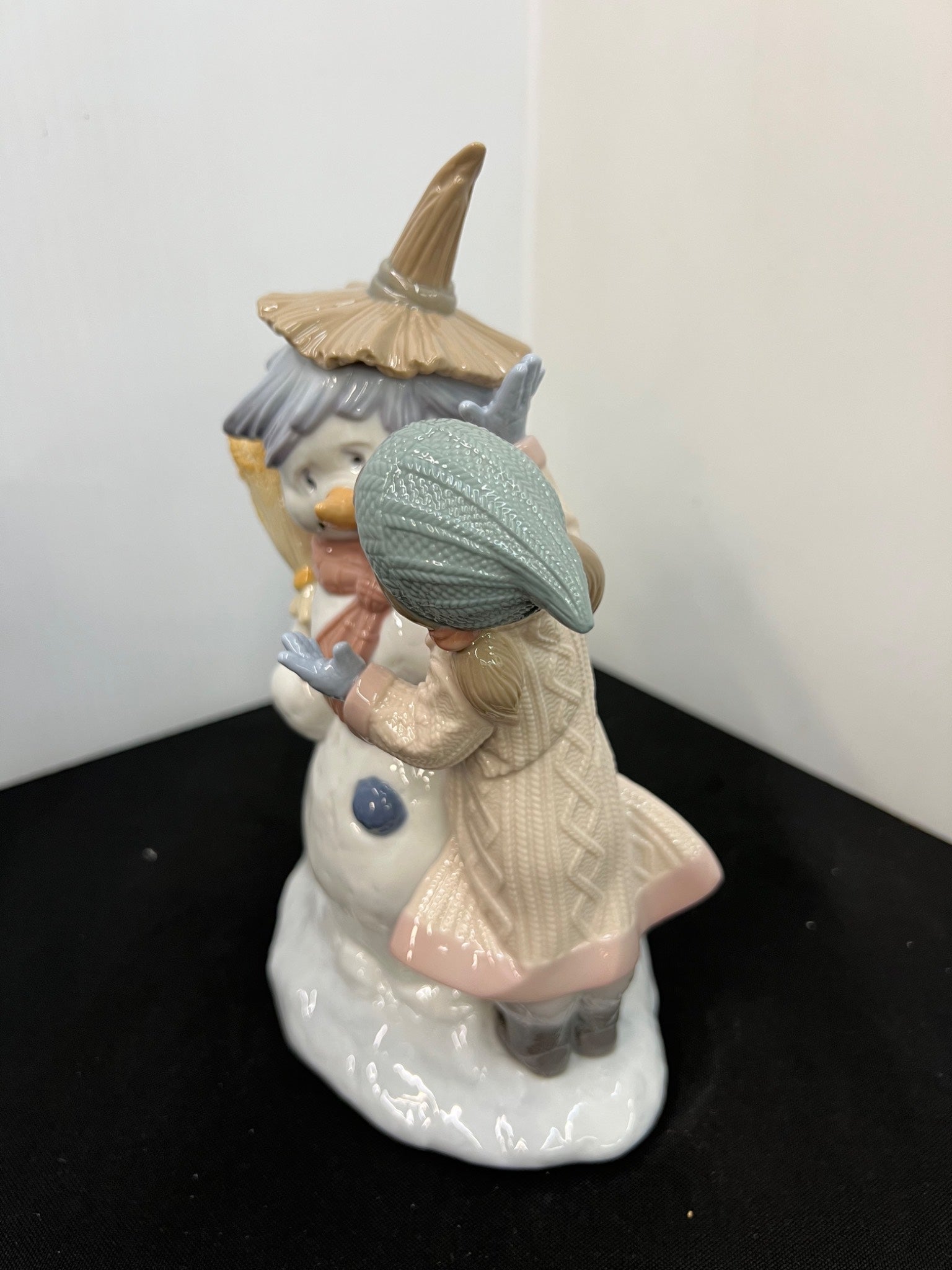 Decorative figurine of a person in a coat and hat interacting with a bird-like creature on a white base.