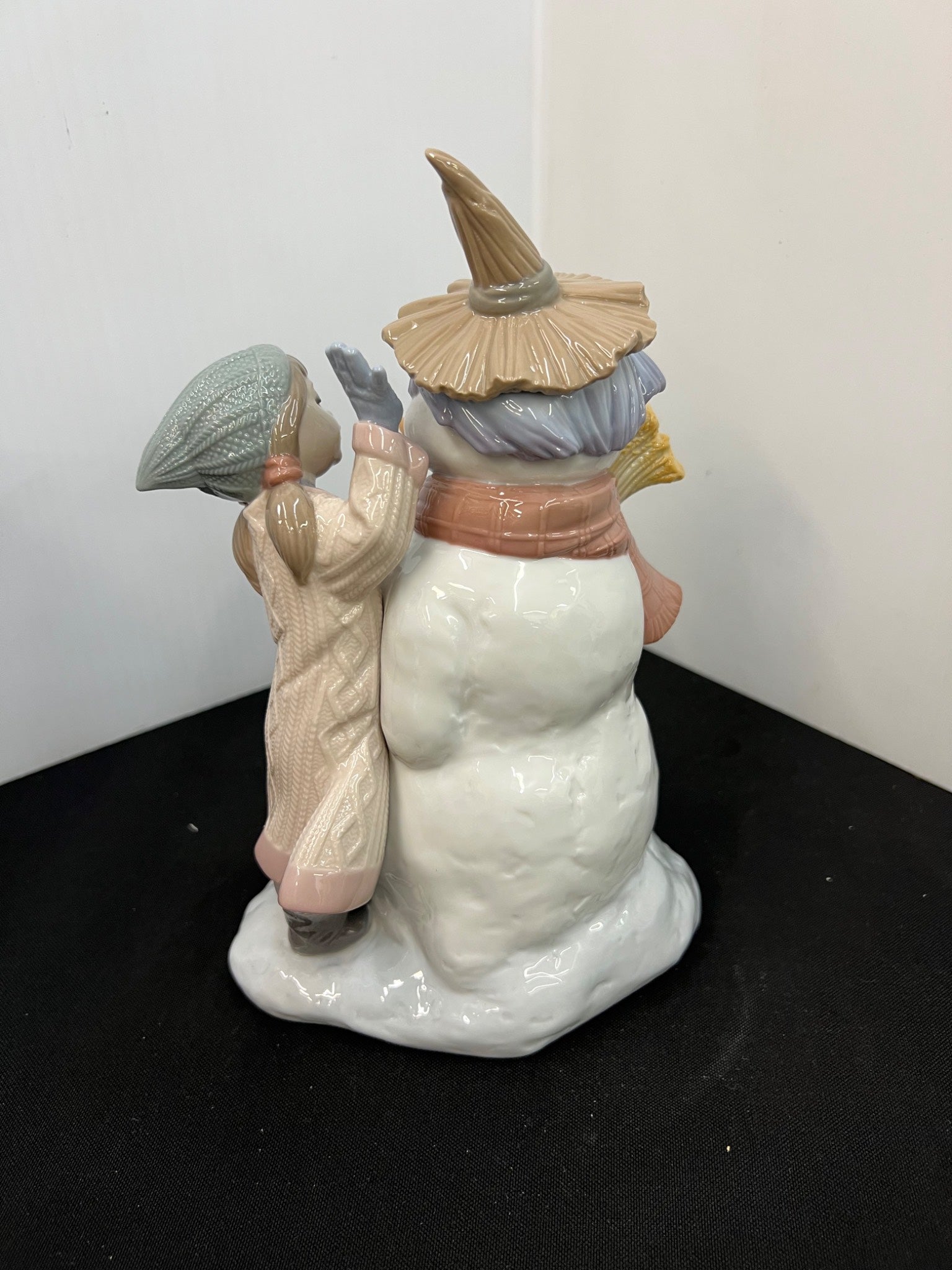 Decorative figurine of a snowman with a child and another figure on a black surface.