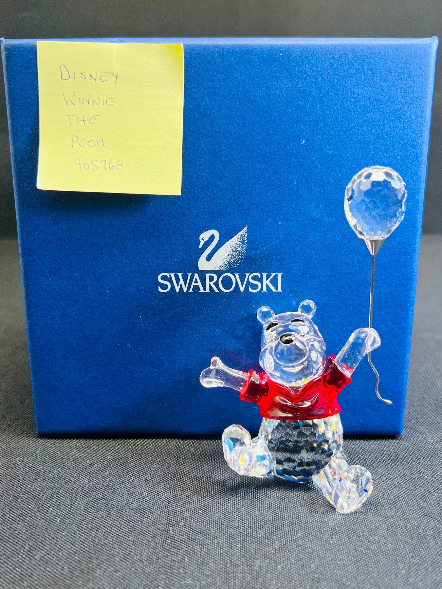 Swarovski crystal figure of a bear with a balloon in front of a Swarovski branded box.