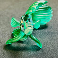 Glass fish figurine with green and clear colors on a textured surface