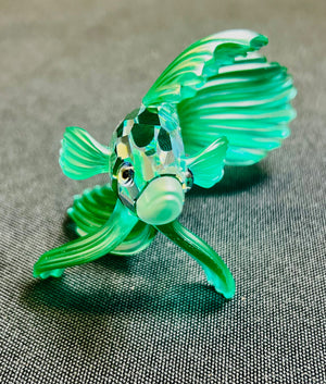 Glass fish figurine with green and clear colors on a textured surface