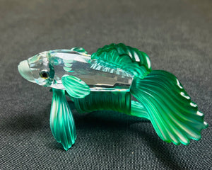Green glass fish figurine on a dark textured surface