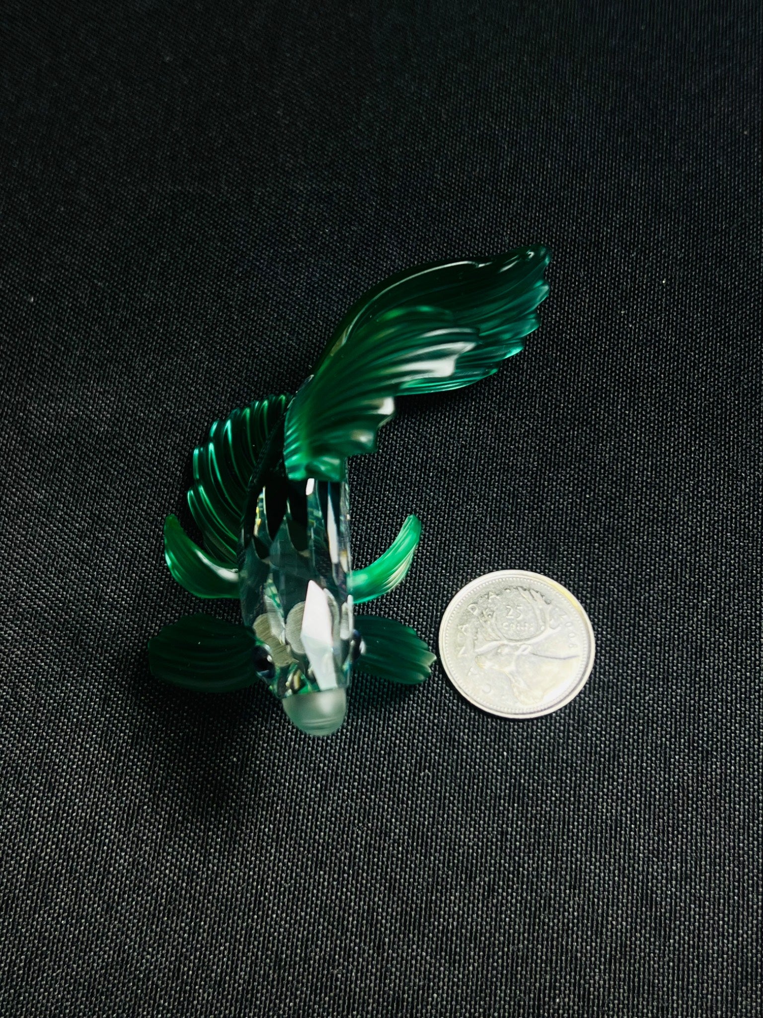 Green glass figurine of a bird on a black background with a coin for scale.
