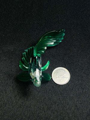 Green glass figurine of a bird on a black background with a coin for scale.