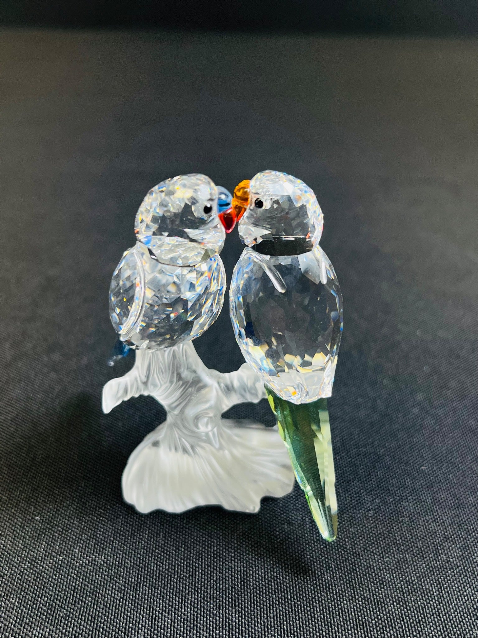 Glass figurine of two parrots on a branch against a dark background