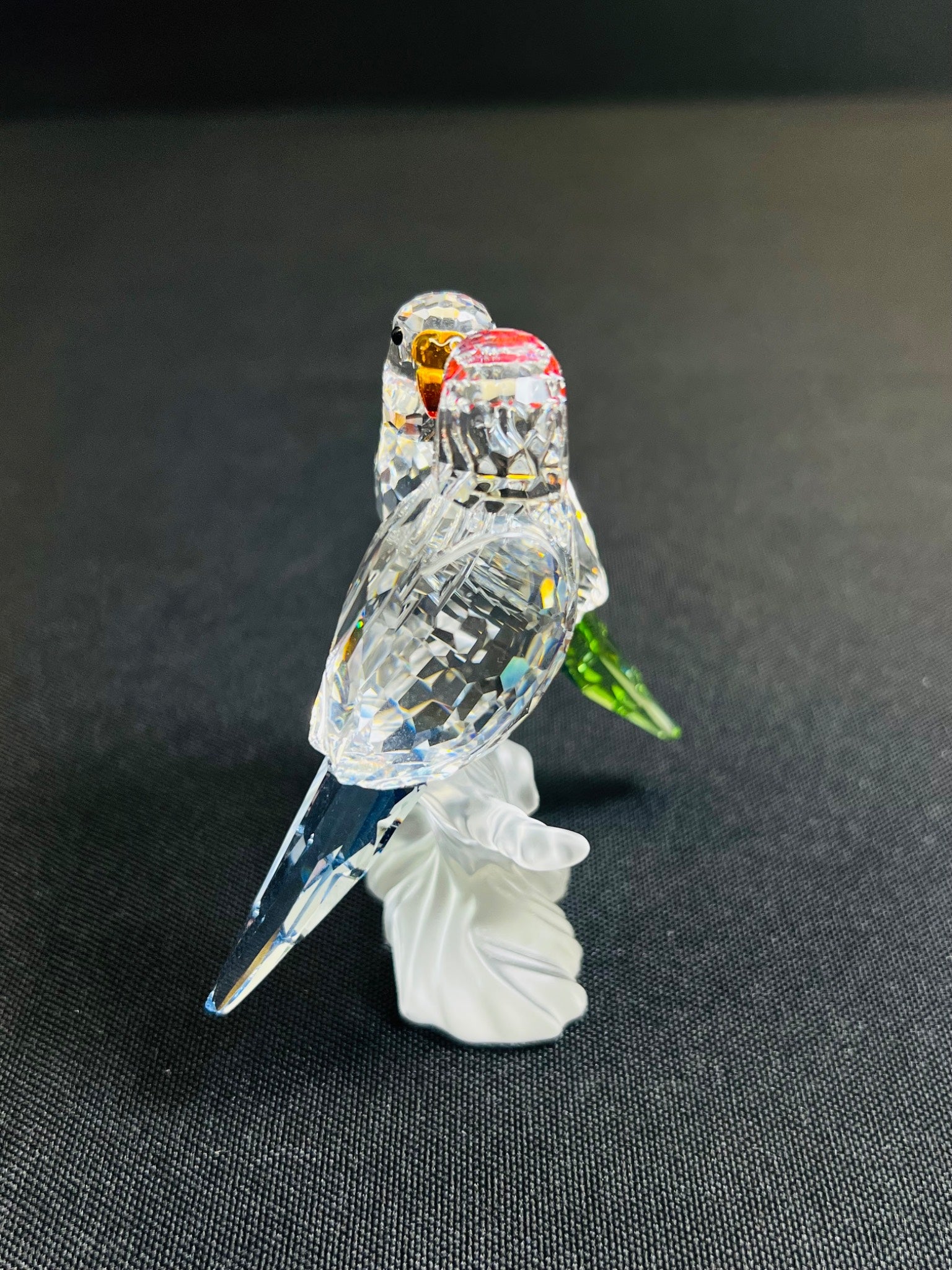 Glass figurine of two birds on a branch with a leaf against a dark background