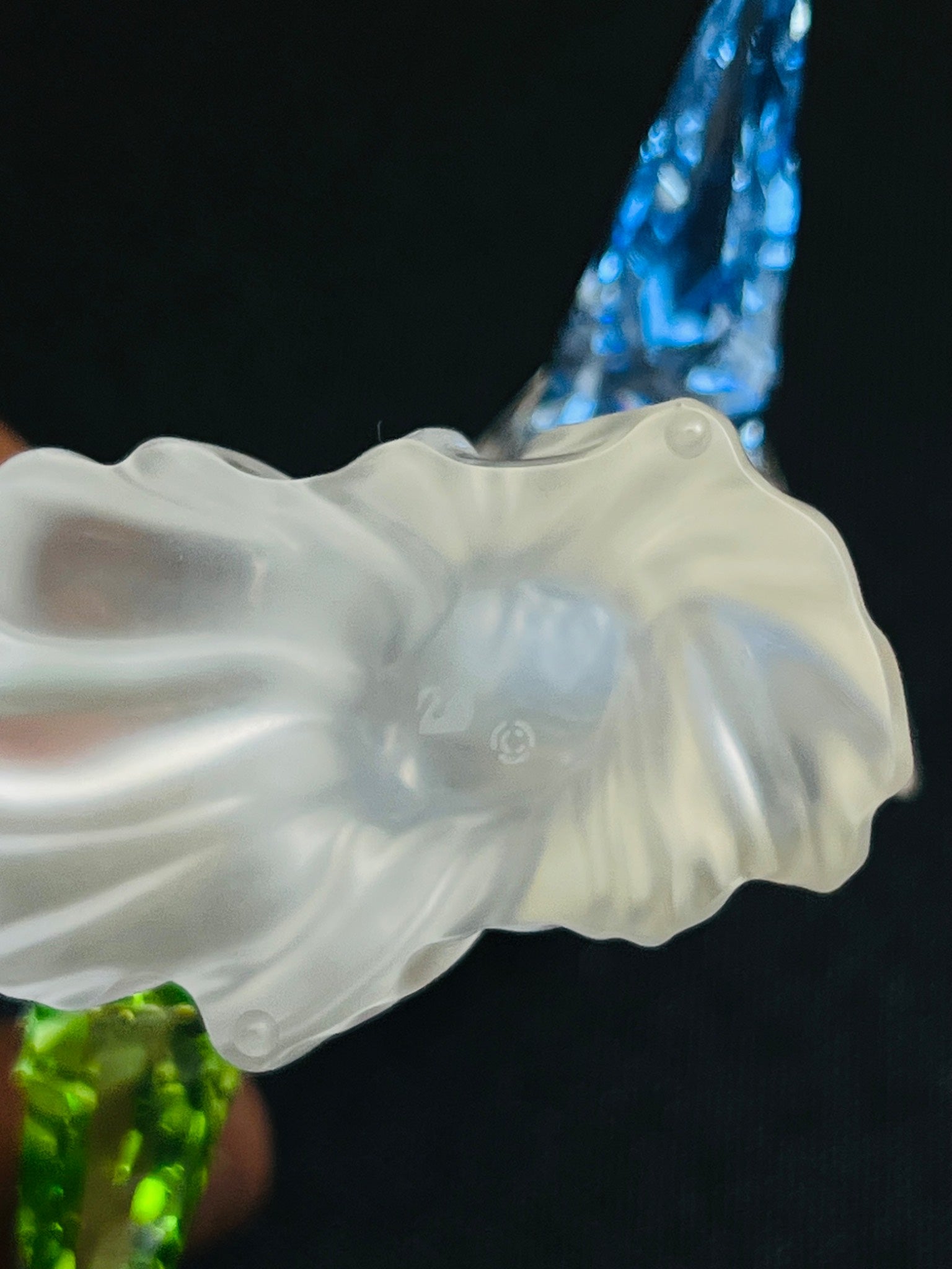 Close-up of a white glass sculpture with a blurred blue and green background