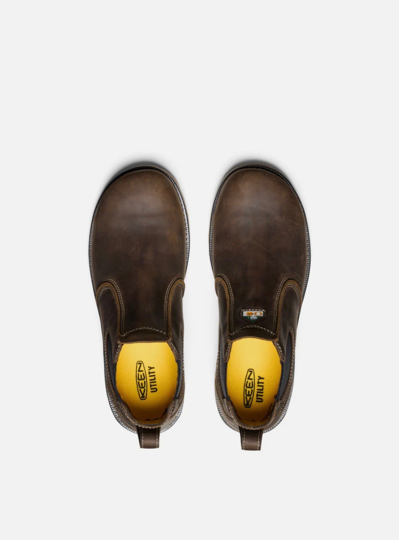Pair of brown Chelsea boots with yellow soles on a white background