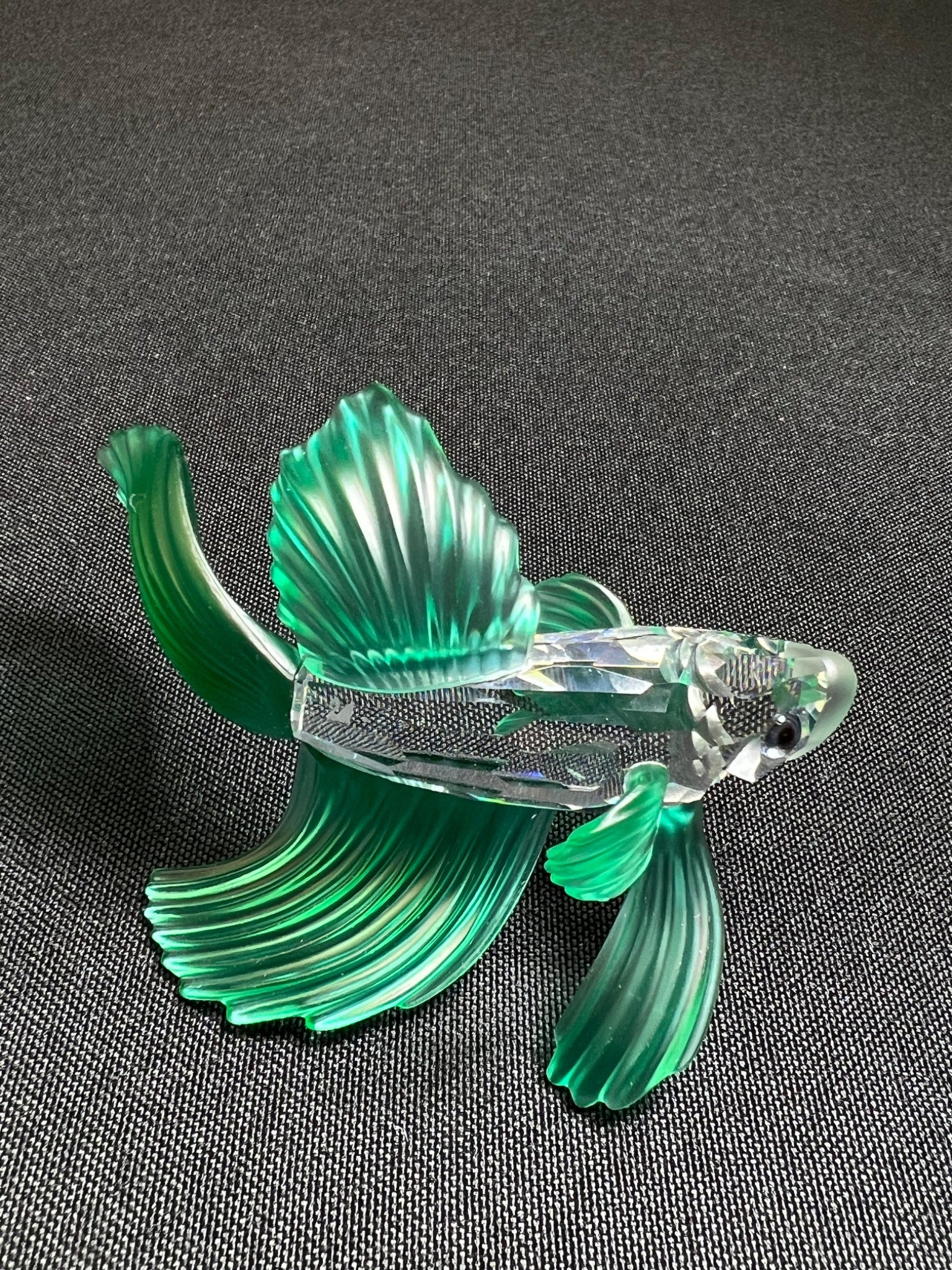 Glass fish figurine with green and clear colors on a dark background