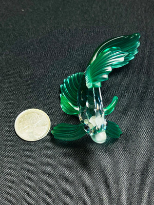 Green glass fish figurine next to a coin on a dark background
