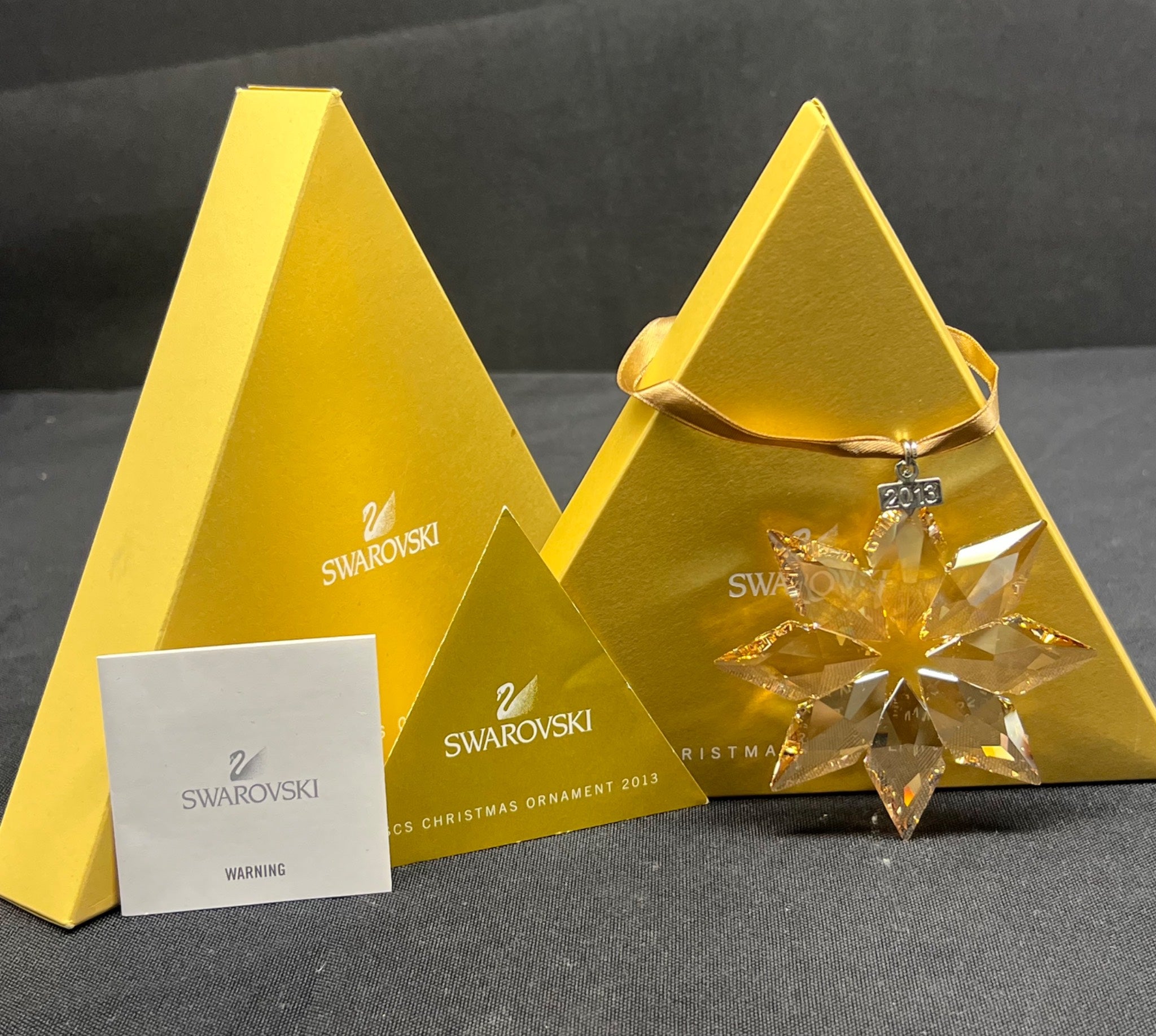 Swarovski crystal Christmas ornament in a pyramid-shaped box on a dark surface.