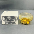 Yellow glass bowl with decorative base next to its packaging on a gray surface