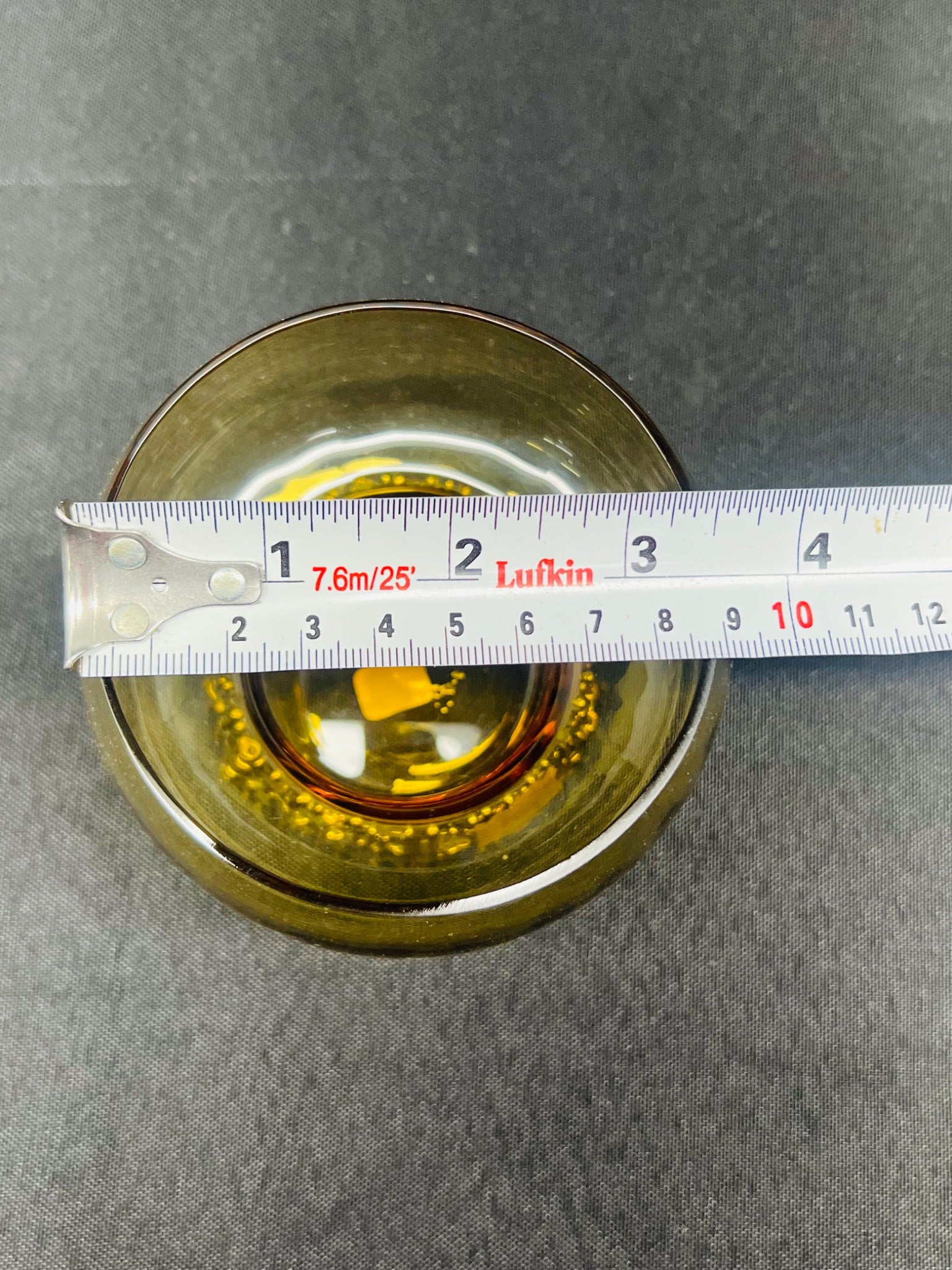 Measuring a round metallic object with a ruler on a gray background
