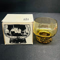 Glass with textured base next to its packaging on a dark surface