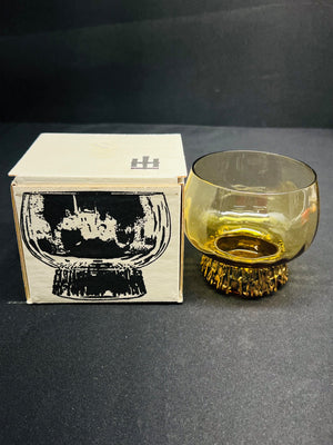 Glass with textured base next to its packaging on a dark surface