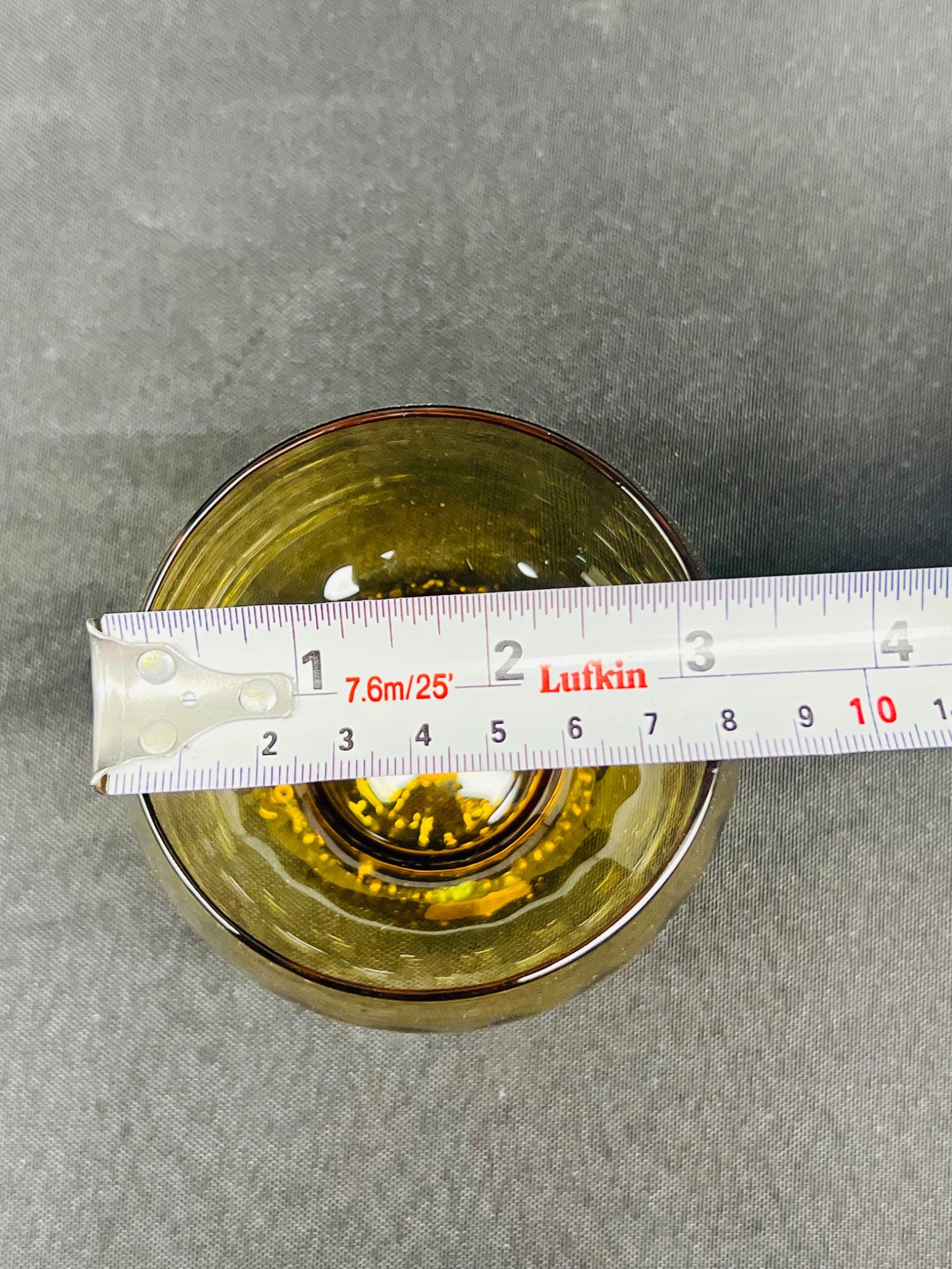 Glass container with a measuring tape showing its diameter on a gray background