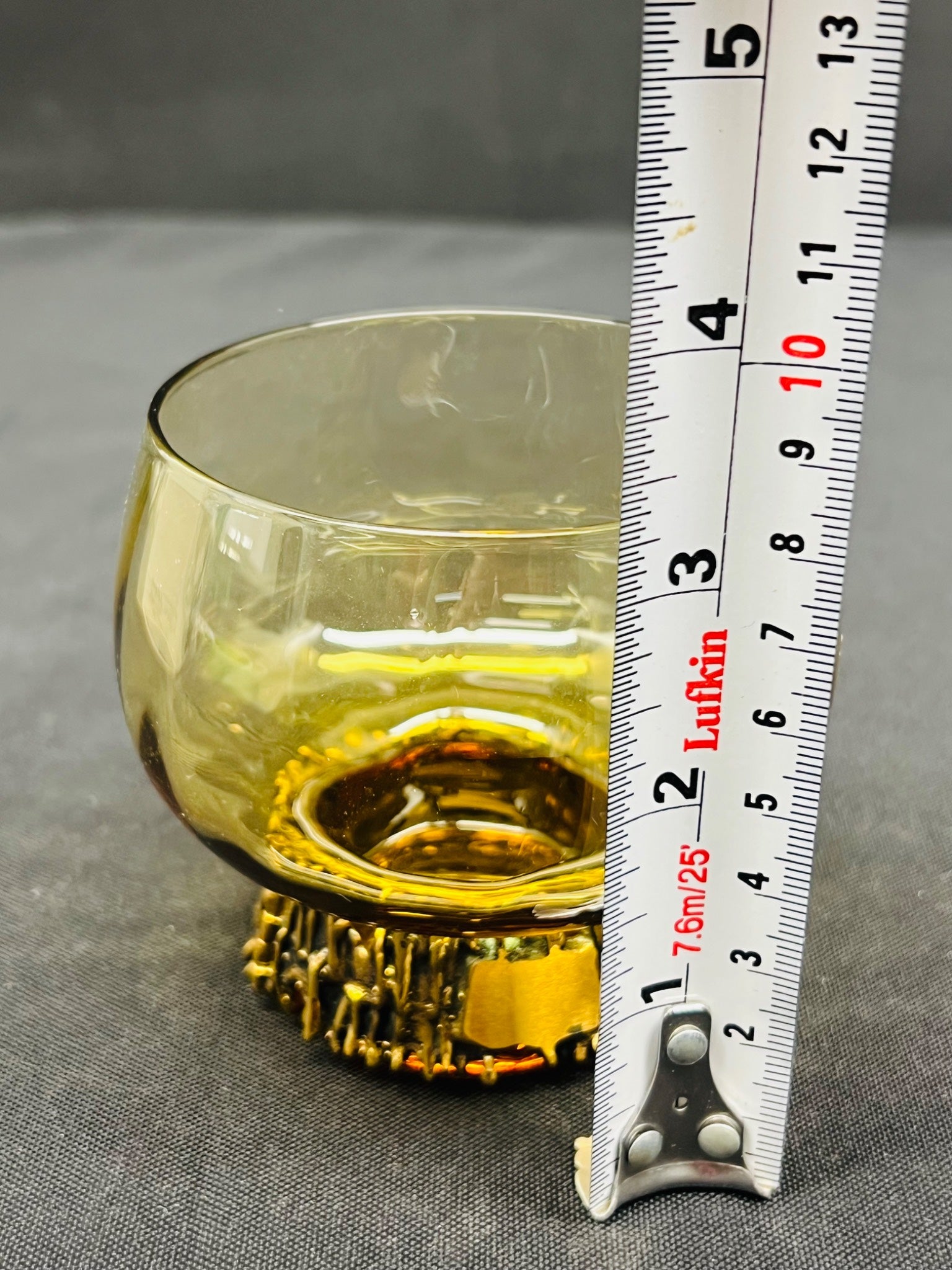 Yellow glass with metal base next to a ruler on a gray surface