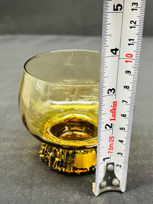 Yellow glass with metal base next to a ruler on a gray surface