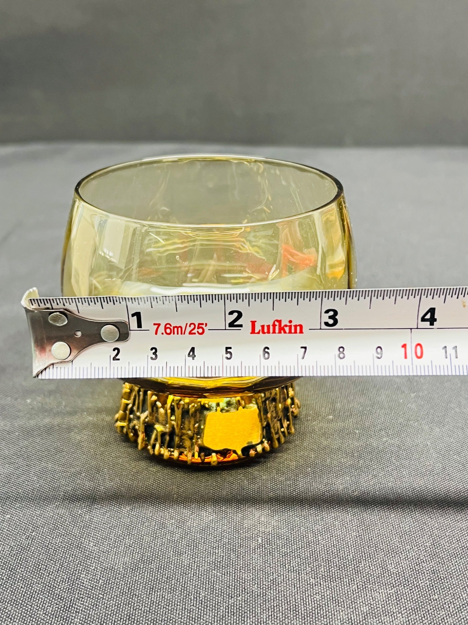 Yellow glass bowl with a measuring tape for scale on a gray background