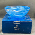 Blue glass bowl on a Kosta Boda branded box against a gray background