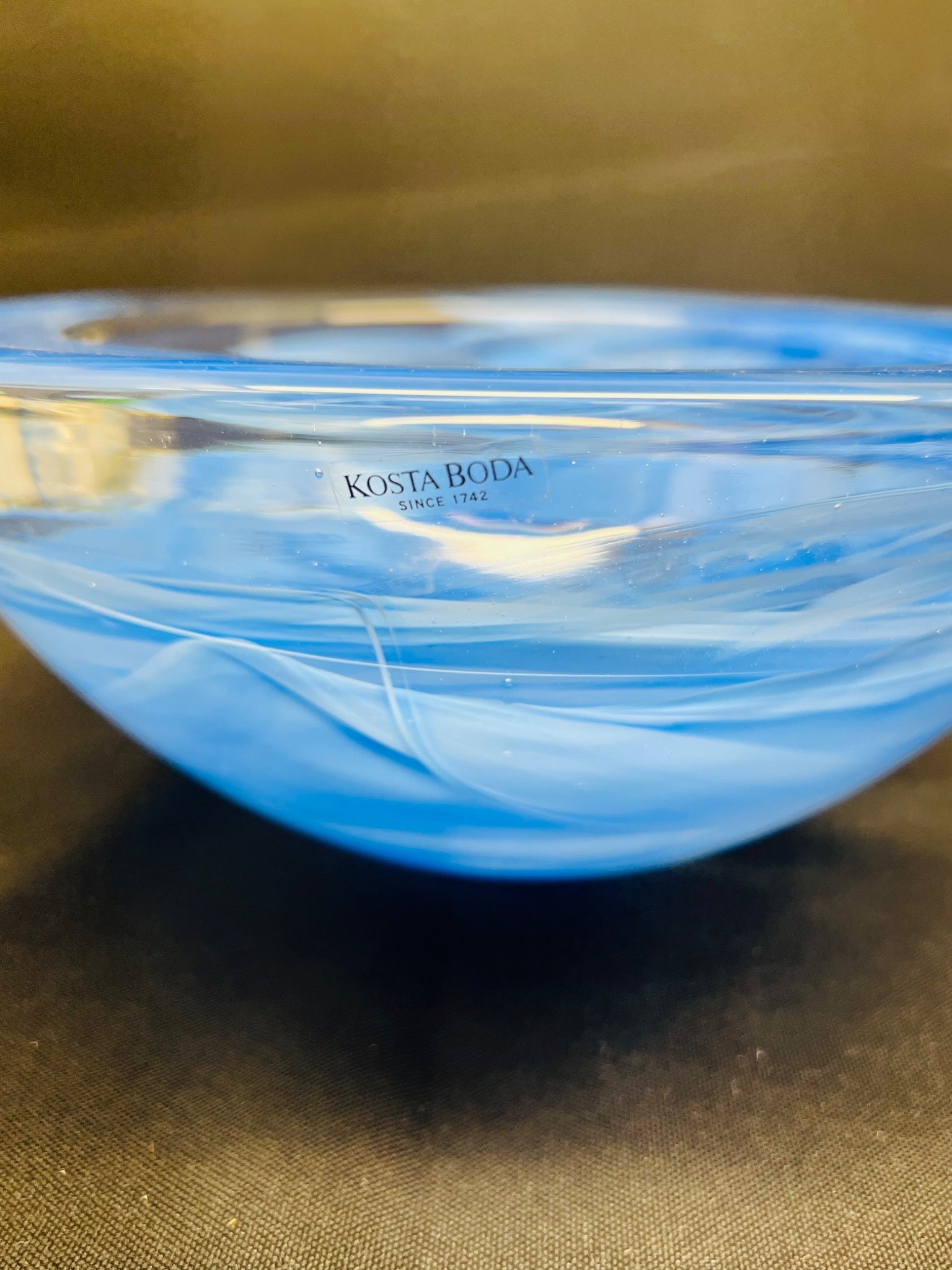 Blue glass bowl with 'Kosta Boda' branding on a brown surface