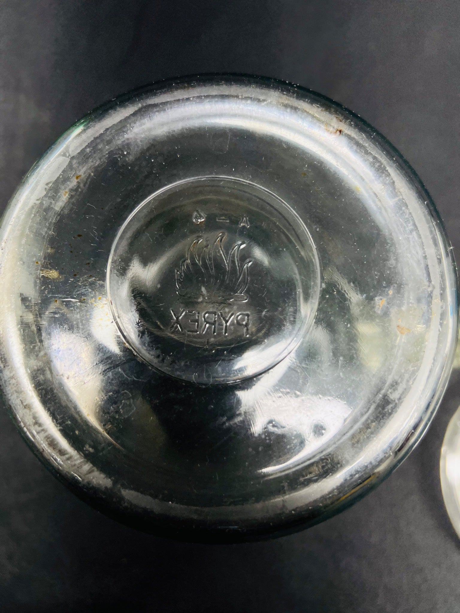 Close-up of a glass container lid with a brand logo on a dark background