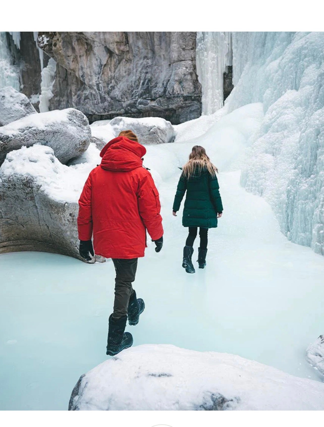 Two people walking through a frozen landscape with ice formations.