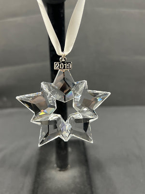 Crystal star ornament with '2019' on a black stand against a gray background