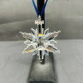 Crystal snowflake ornament on a stand with a blue ribbon against a neutral background