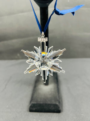 Crystal snowflake ornament on a stand with a blue ribbon against a neutral background