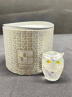 Glass owl figurine in front of a Swarovski branded container on a gray surface