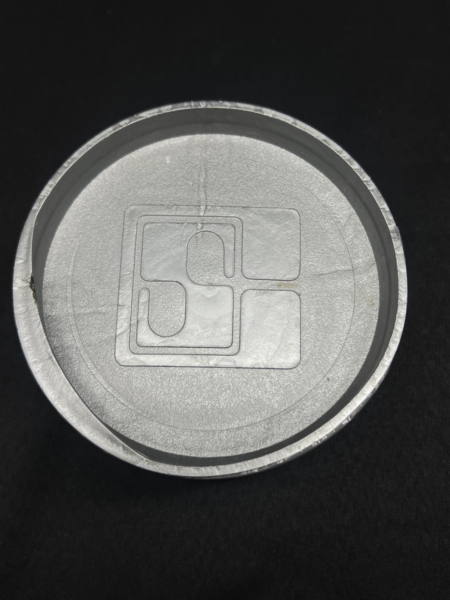 Close-up of a circular metallic object with a central square component on a black background